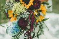 a bold fall wedding bouquet of deep purple dahlias, sunflowers, baby’s breath, greenery of various kinds is a very chic idea