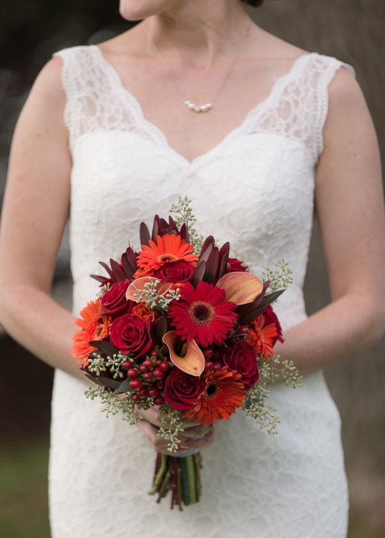 a bold fall wedding bouquet of orange and burgundy gerberas, burgundy roses and orange callas, berries and greenery