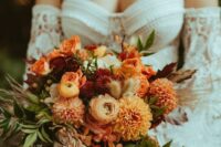 a bold fall wedding bouquet of rust and burgundy dahlias, ranunculus, greenery, berries and some dried flowers for a boho bride