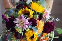 a bold fall wedding bouquet of sunflowers, pale pink, burgundy blooms, berries, eucalyptus and thistles is gorgeous