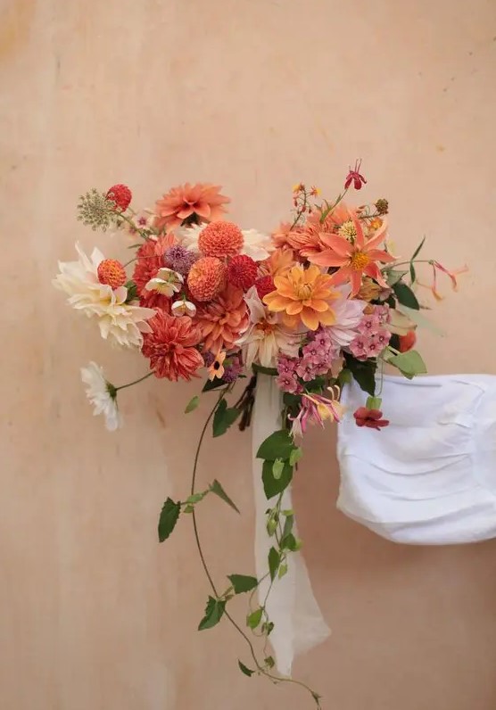 a bold fall wedding bouquet with orange, burnt orange and deep red and pink blooms and some cascading greenery
