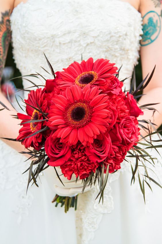 a bold wedding bouquet of deep red gerberas and roses, some peonies and twigs is a catchy idea for a Halloween wedding