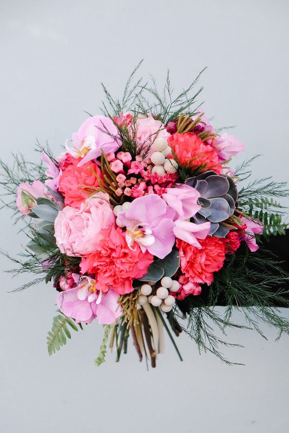 a bold wedding bouquet of pink and coral carnations, pink orchids, fillers, berries, succulents and some greenery