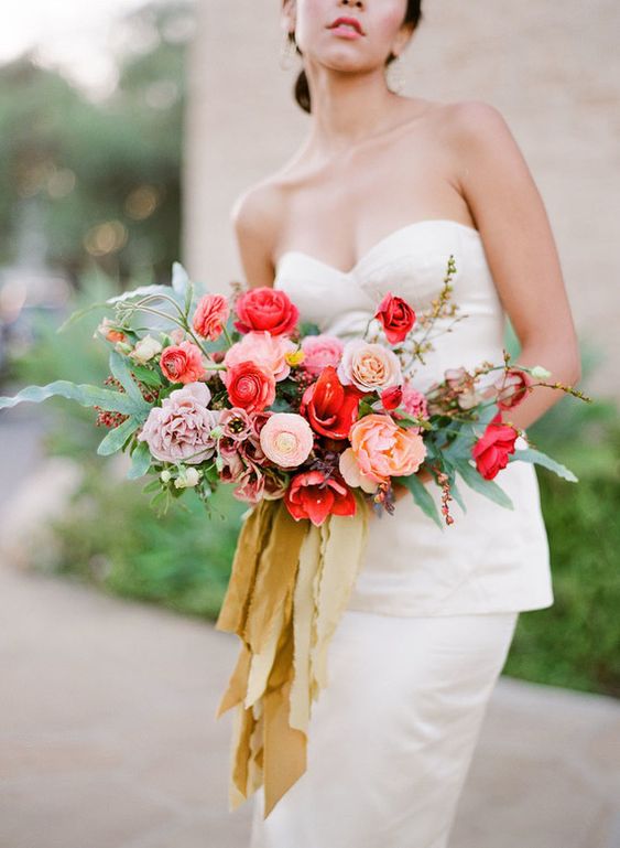 a bold wedding bouquet of red roses, blush roses, mauve and peachy carnations, greenery and twigs and some mustard ribbons