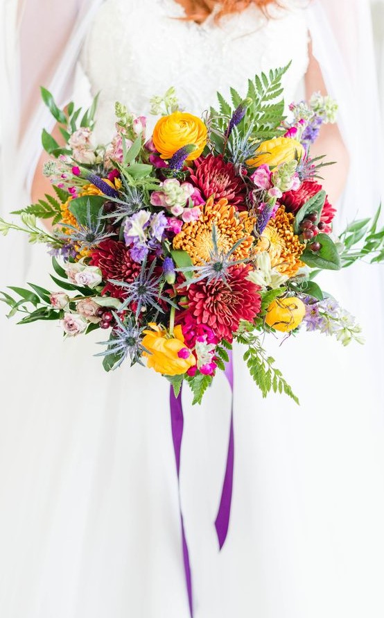 a bold wedding bouquet with yellow, burgundy, purple blooms, greenery, astilbe and purple ribbons is fun