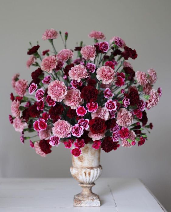 a bold wedding centerpiece of a tall urn with pink, fuchsia and burgundy carnations will be great for a Valentine's Day wedding