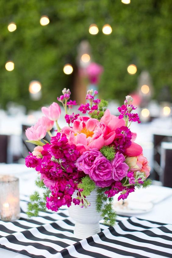 a bold wedding centerpiece of bright fuchsia blooms including carnations and peonies and some greenery is a lovely idea