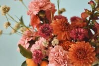 a bold wedding centerpiece of pink carnations, orange and bold pink dahlias, citrus, some seed pods and leaves