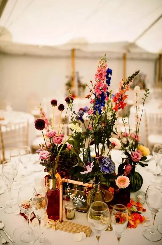 a bold wedding centerpiece of violet, pink, yellow, orange and blue blooms including roses, dahlias and allium is wow