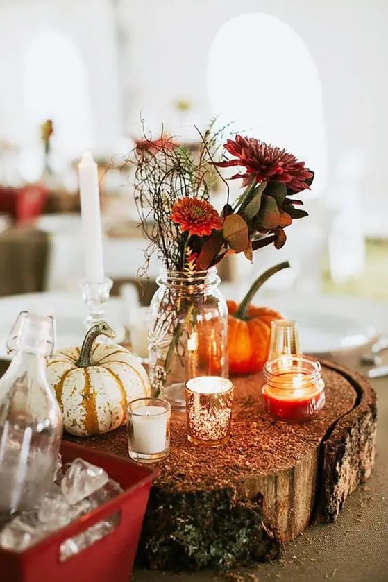 a bright and simple fall rustic wedding centerpiece of a wood slice with glitter, candles, pumpkins, burgundy blooms and greenery