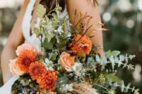 a bright and textural wedding bouquet with orange dahlias, some neutral and blue blooms, textural greenery, grass and twigs