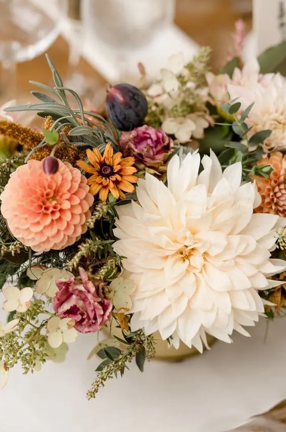 a bright fall wedding centerpiece of pink, yellow blooms, white and orange dahlias, dried flowers and greenery, figs
