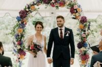 a bright floral wedding arch with lilac, yellow, blush, pink, orange and white blooms and some greenery is very chic