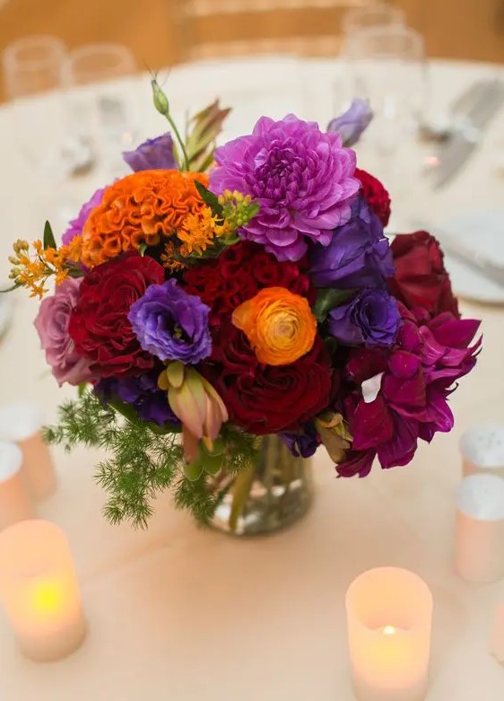 a bright jewel tone wedding centerpiece of orange, purple, violet, burgundy and fuchsia blooms and some greenery