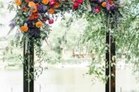 a bright wedding arch featuring purple, yellow, orange and hot pink blooms, greenery and pampas grass for a bold fall wedding