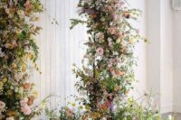 a bright wedding arch with greenery, pink, blush, yellow blooms and blooming branches is a lovely idea