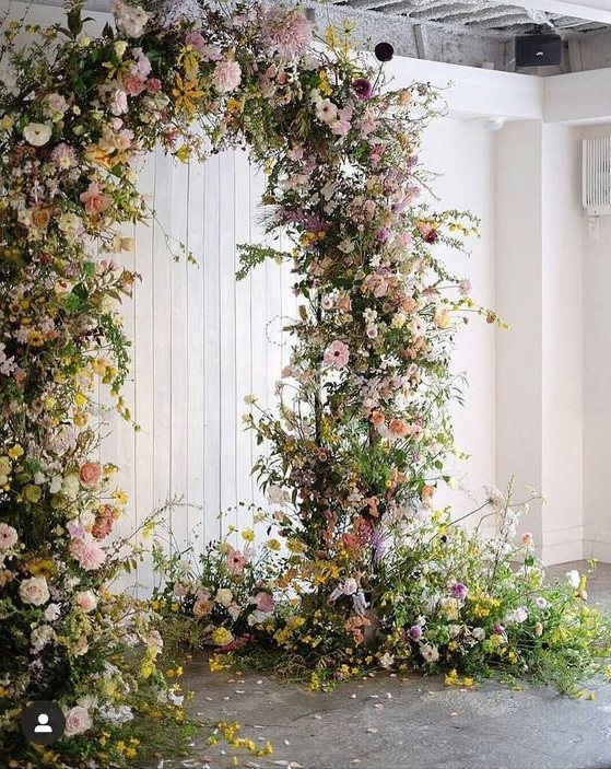 a bright wedding arch with greenery, pink, blush, yellow blooms and blooming branches is a lovely idea