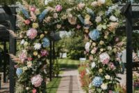 a bright wedding arch with plenty of texture, with greenery, pink and blue hydrangeas, pampas grass and some roses and dahlias