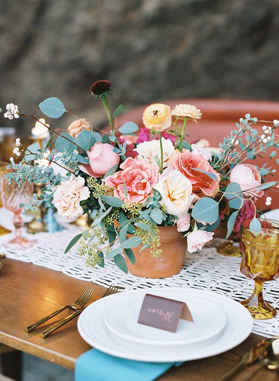 a bright wedding centerpiece of neutral and pastel blooms, carnations, peony roses and ranunculus, greenery and berries