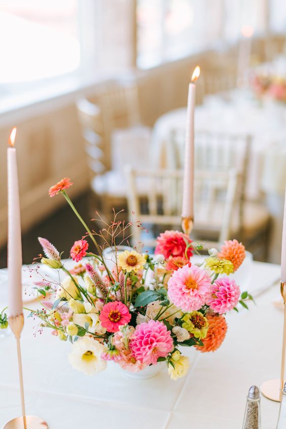 a bright wedding centerpiece of pink and orange dahlias, yellow and hot pink blooms, astilbe and some greenery for a summer wedding