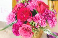 a bright wedding centerpiece of red roses and peony roses, pink roses and carnations, greenery in a gold vase is a bold and cool idea