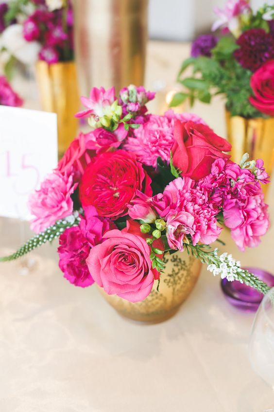 a bright wedding centerpiece of red roses and peony roses, pink roses and carnations, greenery in a gold vase is a bold and cool idea