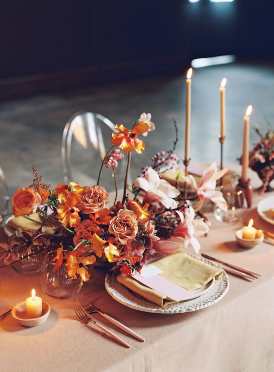 a catchy modern wedding centerpiece of rust-colored blooms, leaves and dusty pink carnations plus candles around is wow