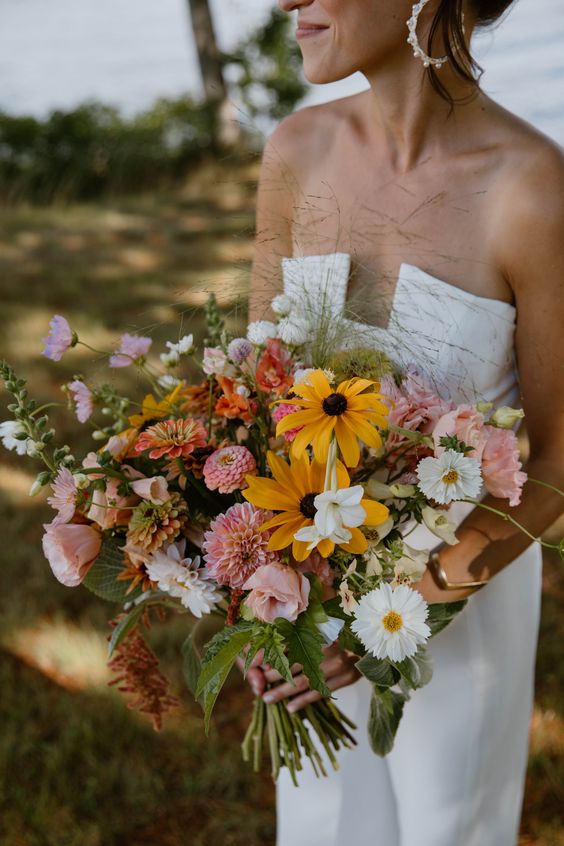 a catchy wedding bouquet of pink dahlias, some orange, white and yellow blooms and greenery for a summer wedding