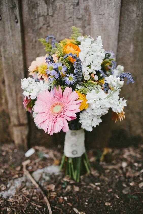a cheerful wedding bouquet of pink and orange gerberas, white hydrangeas, some yellow ranunculus, purple fillers for a rustic bride