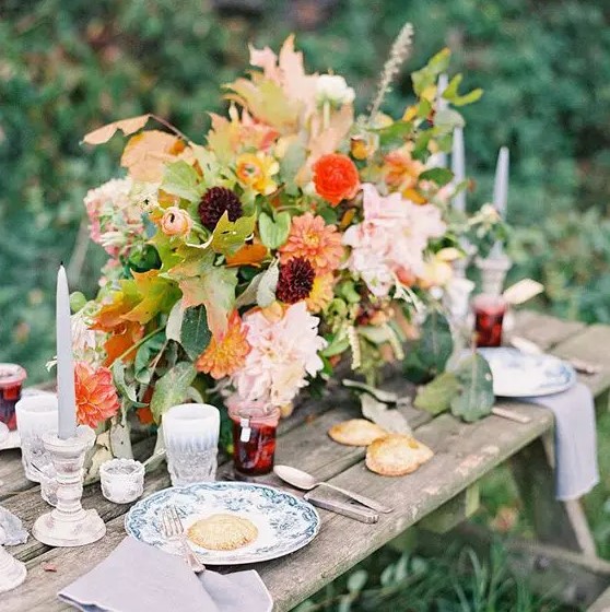 a chic and cool rustic fall wedding tablescape with lush and bright florals, greenery, deep purple and orange blooms, grey candles, printed plates and homemade jam as favors
