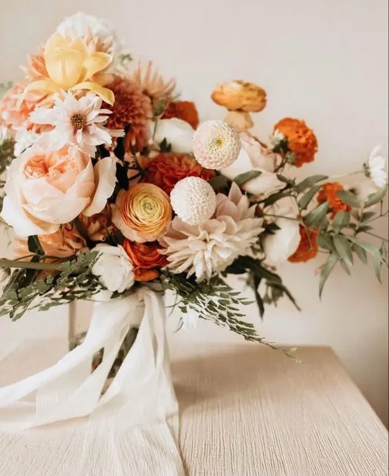 a chic fall wedding bouquet of white dahlias, blush peonies and white and orange peony roses, some white roses, greenery and white ribbons