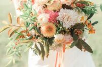 a chic fall wedding bouquet of yellow and pink dahlias, white roses, yellow ranunculus, beerries, greenery and fall leaves
