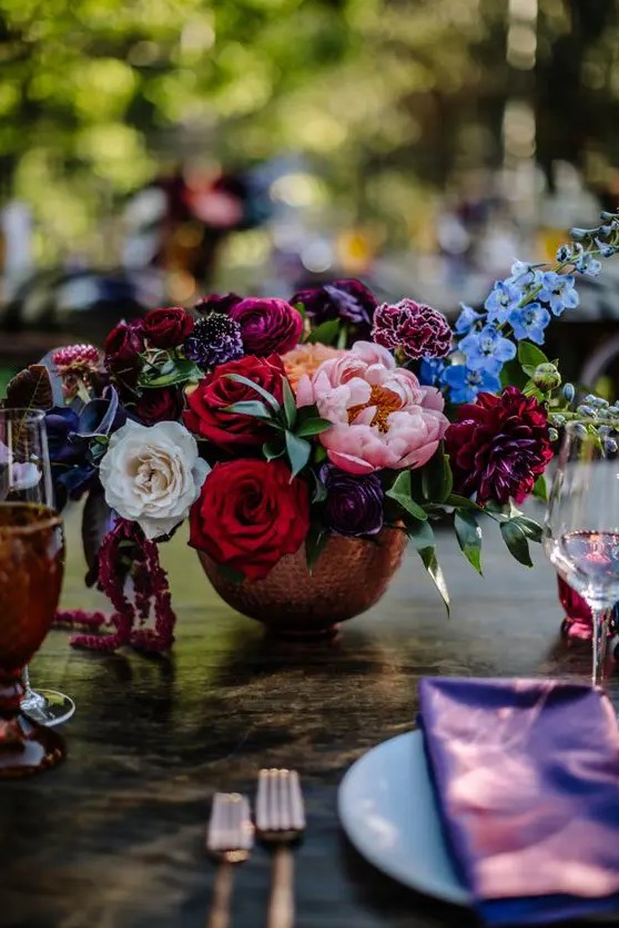 a chic jewel tone wedding centerpiece of deep red, blush, purple, burgundy and blue blooms and greenery is a lovely idea for the fall