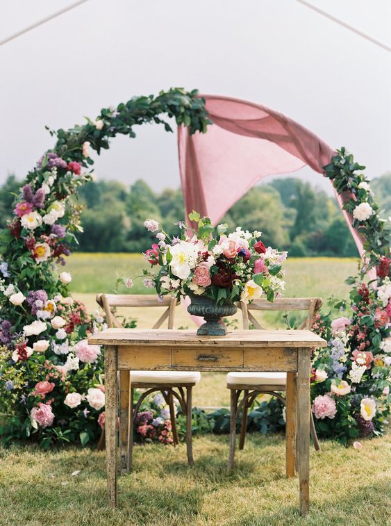 a chic round wedding arch with blush, blush, pink and purple blooms including peonies and mauve fabric is great
