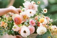 a chic summer wedding centerpiece of neutral and pink dahlias, yellow and orange blooms and greenery in a refined urn