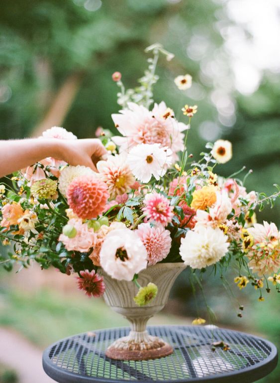 a chic summer wedding centerpiece of neutral and pink dahlias, yellow and orange blooms and greenery in a refined urn