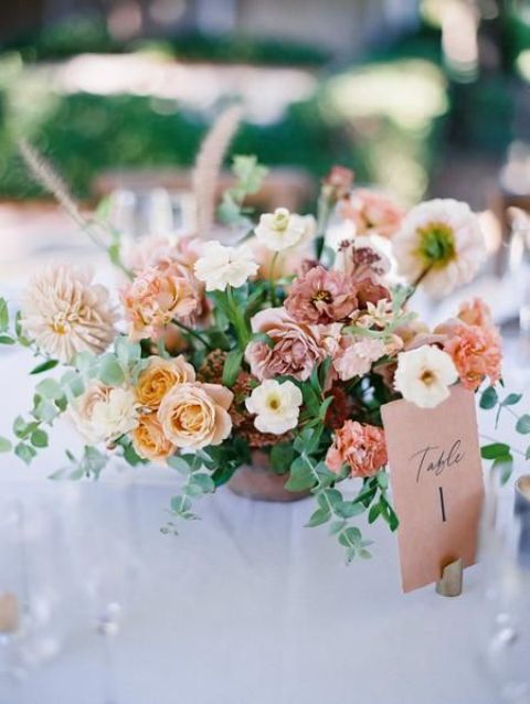 a chic terracotta wedding centerpiece of neutra pale yellow and blush blooms including carnations, greenery and a table number