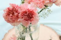a chic wedding centerpiece of pink carnations and baby’s breath plus a tree slice is a lovely idea for a rustic wedding