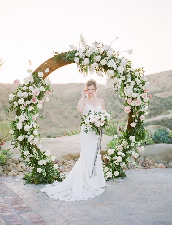 a circle spring wedding arch decorated with lush greenery and white and pink blooms is a trendy idea