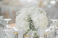 a classic white wedding centerpiece of white hydrangeas and baby’s breath, candles around is a catchy idea for spring or summer