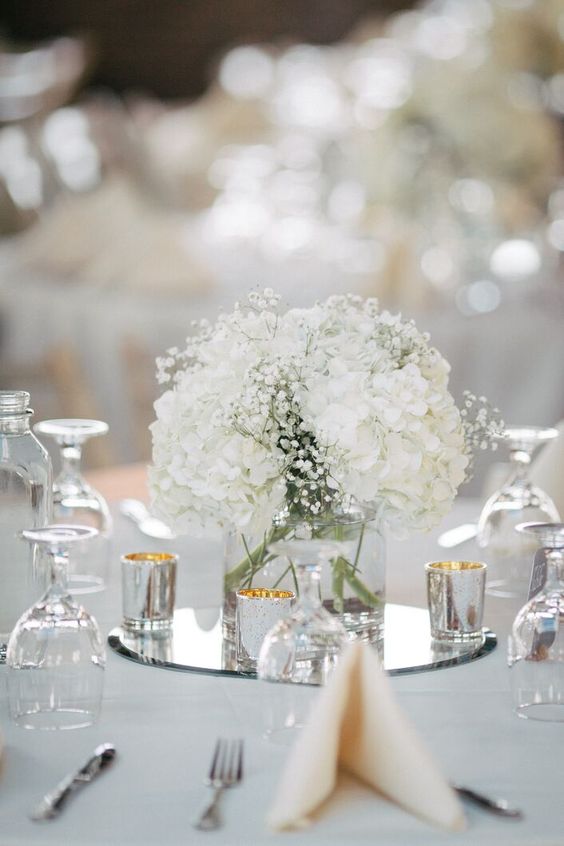 a classic white wedding centerpiece of white hydrangeas and baby's breath, candles around is a catchy idea for spring or summer