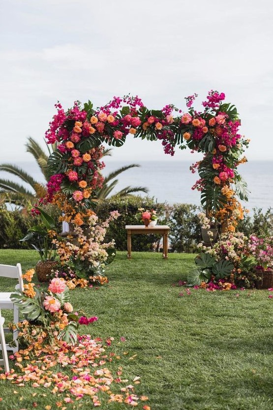 a color block wedding arch with tropical leaves, hot pink, orange, yellow and blush blooms for a tropical wedding