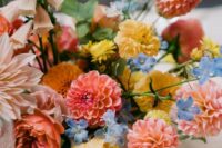 a colorful and dimensional wedding centerpiece of pink and fiery red dahlias, yellow and orange blooms, blush ones and blue ones for a bold wedding