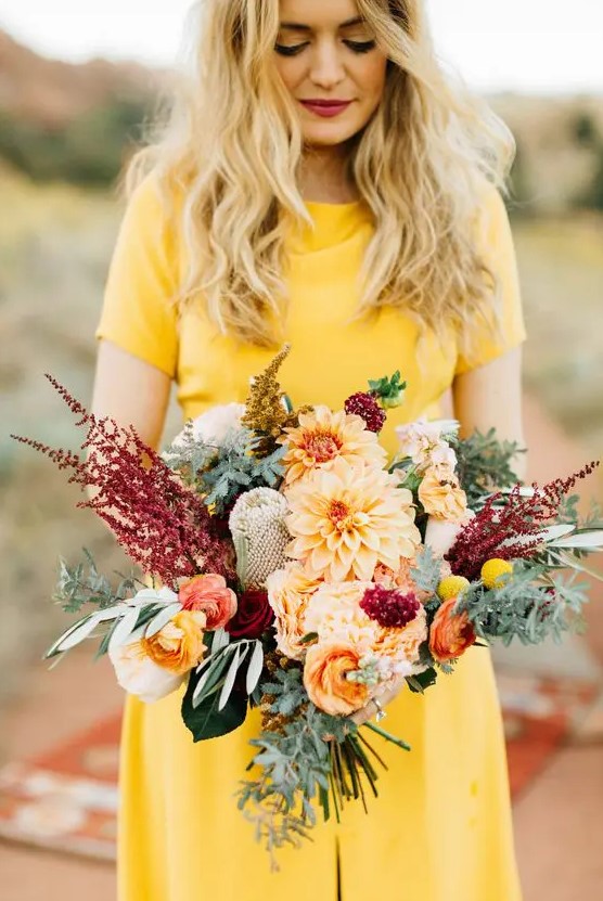 a colorful autumn wedding bouquet of orange dahlias, orange and red ranunculus, greenery, bold blooms and leaves
