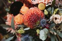 a colorful fall wedding bouquet of yellow roses, orange and pink dahlias, deep purple blooms, greenery and thistles is wow