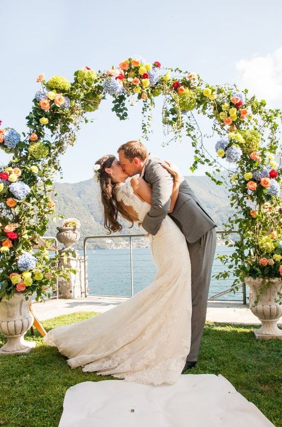 a colorful round wedding arch coming out of vintage urns, with greenery, green, blue, yellow, peachy and red blooms makes a statement