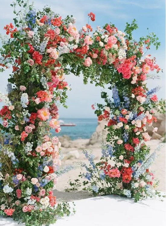 a colorful summer wedding arch with pink, red, coral, blue and white blooms and greenery is amazing for a bright wedding