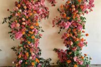 a colorful wedding altar with greenery, orange and pink mums, pink peonies and other blooms for a bold wedding