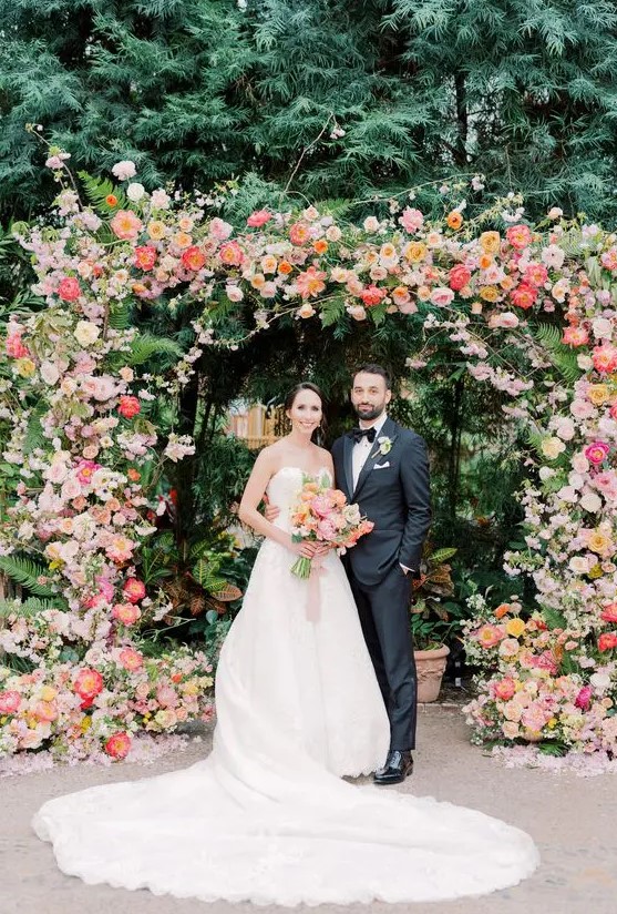 a colorful wedding arch decorated with greenery, blush, coral and pink blooms is a bold idea for a colorful summer wedding