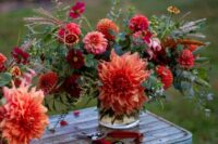 a colorful wedding arrangement of red and coral dahlias and greenery plus some grasses for summer or fall
